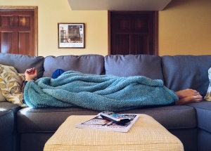 Cold person laying on the couch under a blanket.