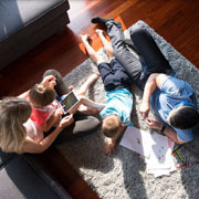 Family laying on the living room floor, coloring papers with young children.