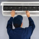 Air conditioning service repair person working on mini-split air source heat pump interior unit.