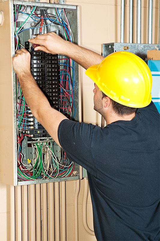 Electrician installing and adjusting electrical control panel in a commercial building.