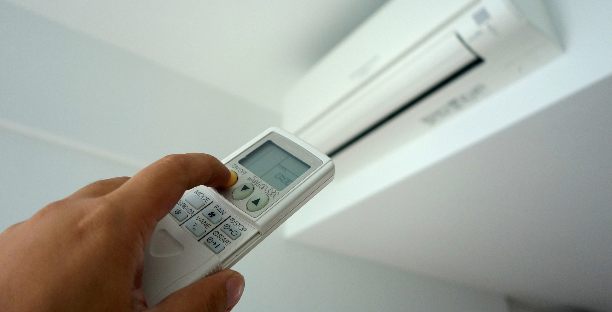 A person using a remote control to adjust their mini-split heat pump air conditioning settings.