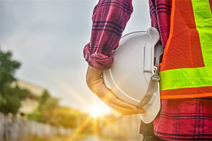 Contractor in high-visibility vest holding helmet facing the sunset