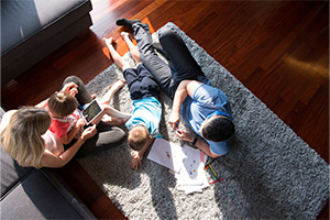 Family laying on the living room floor, coloring papers with young children.