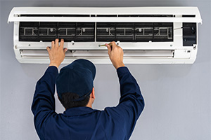 Air conditioning service repair person working on mini-split air source heat pump interior unit.