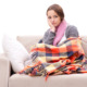 Teenager suffering from heating system failure sitting on coach in the cold with a blanket and scarf.